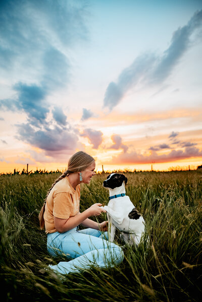 Woman shakes with dog in field at sunset