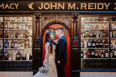 Bride holding back of groom's neck in front of a red arch door