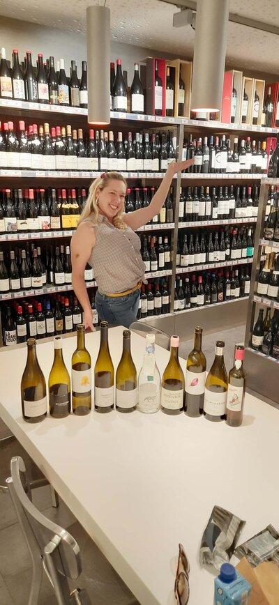 Maria Cristina Barrero posing in front of wine shelves with bottles of wine placed on the table in  the foreground.