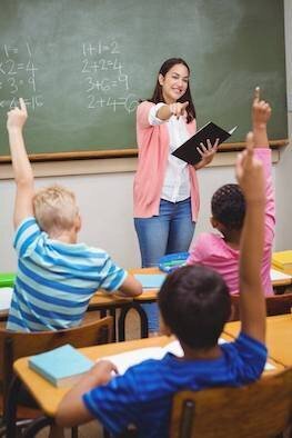 Female teacher engaging with students raising their hands in a classroom setting.