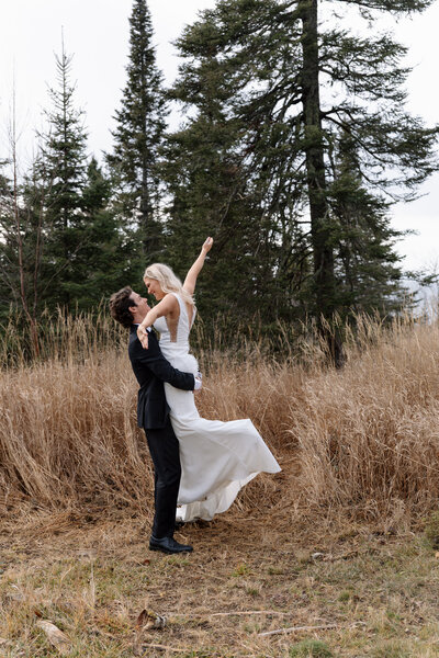 Playful moment as the groom holds the bride in the air, celebrating their elopement surrounded by nature.