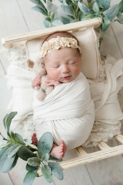 Newborn baby girl is sleeping in a tiny wood bed with a floral headband and holding a tiny bunny during her Pittsburgh newborn session in Bridgeville.