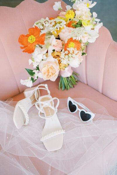 Wedding shoes, bouquet, veil, and heart sunglasses sitting on a pink chair arranged by Austin wedding photographer