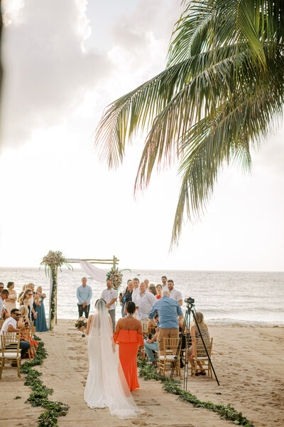 wedding ceremony on a beach surrounded by palm trees, bride walking down the aisle