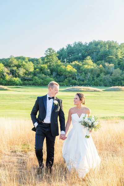 bride and groom walking through tall grass in new england boston