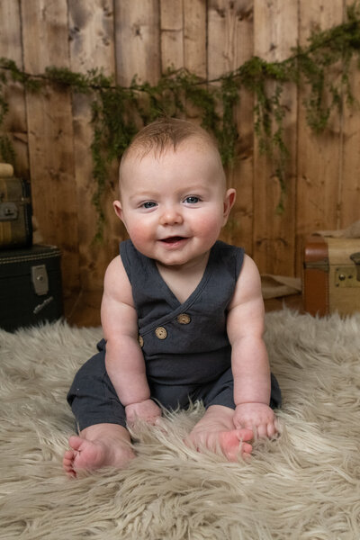 Happy  baby sitting up in front of wooden backdrop