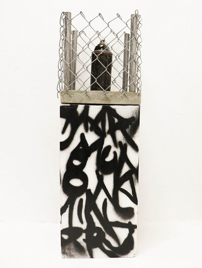 A can of spray paint sits on a pedestal spray painting with abstract graffiti letters, surrounded by a chain link fenced cage