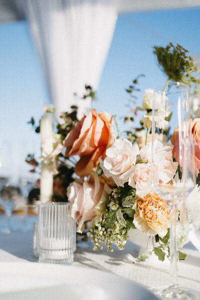 Close up of a centerpiece with a mix of peach, pink, orange, and red florals, next to a small candle in a ribbed glass carousel jar