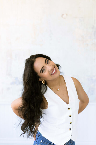 dark haired girl smiling and posing wearing a white top and blue jeans
