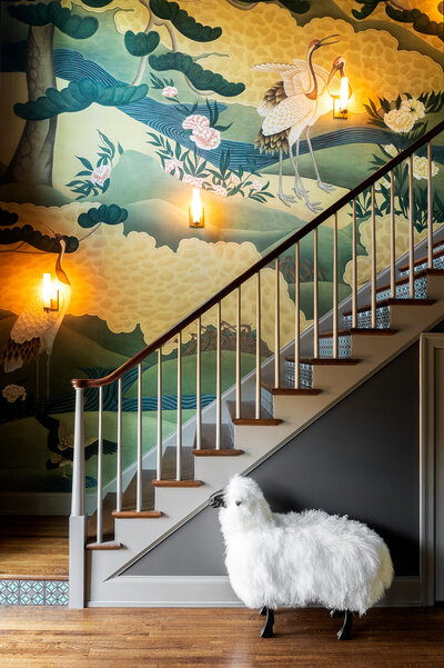 stairway with colorful landscape wallpaper with sconces and a white decorative sheep