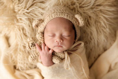 Newborn photographer, a baby sleeps dressed as a teddy bear holding a bear
