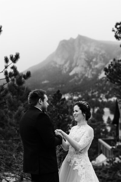 Bride smiles and holds groom's hand with Rocky Mountains  behind them