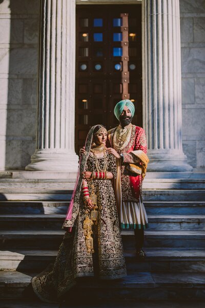 Sikh bride and groom in traditional punjabi outfits standing in front of a white column building at princeton university