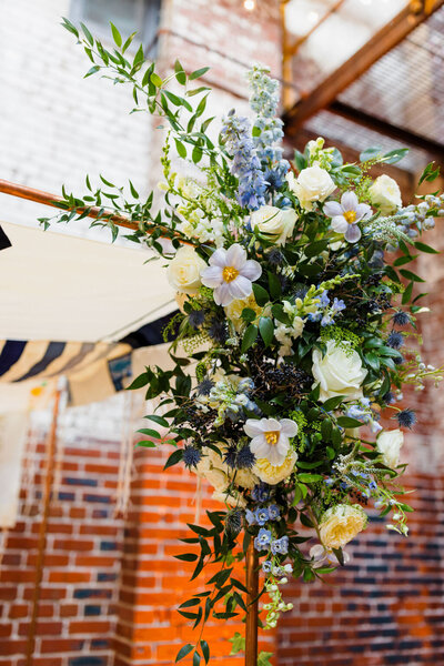 Full, lush greenery and bold flowers on this wedding arch with an industrial brick backdrop.