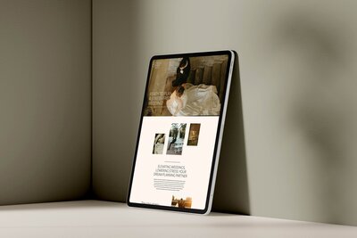 A tablet displaying a Showit web design with images and text leans against a light-colored wall on a flat surface.