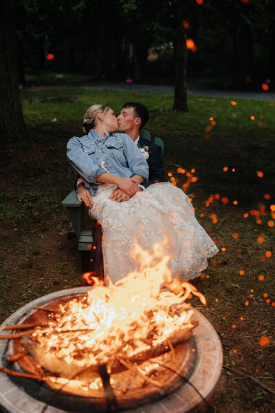 bride and groom kissing while sitting in front of a bonfire