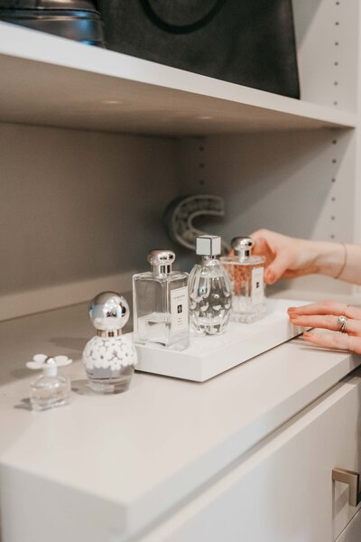 A hand organizing a series of perfumes on a closet shelf