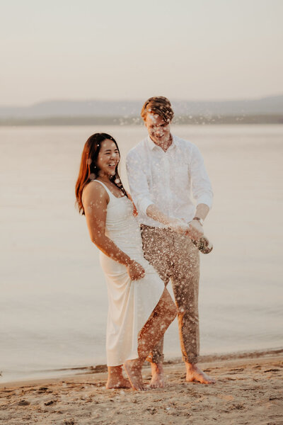 Couple popping champagne on beach