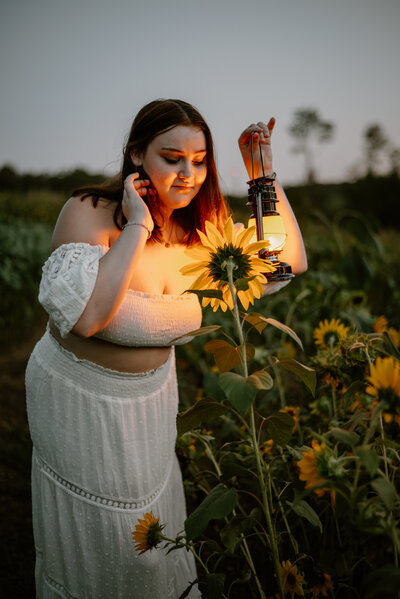 Senior photo of girl holding lantern and smelling sunflower while sun is setting in Maryland.