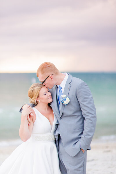 Groom hugging and kissing bride on the beach