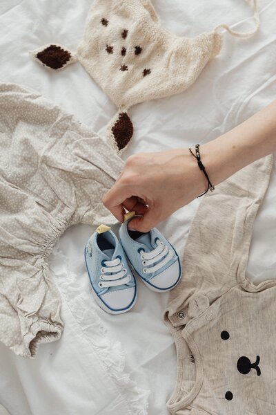 Small blue baby shoes and newborn clothing on bed