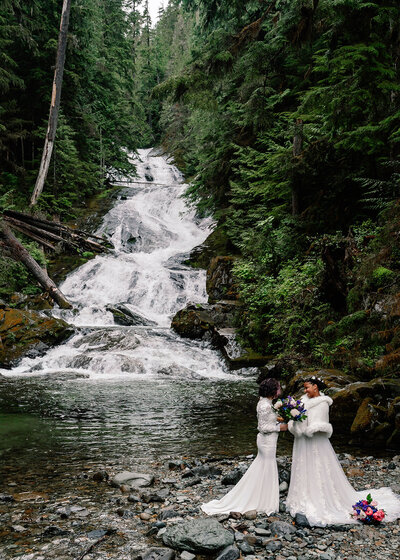 two brides embrace in front of a cascading waterfall during their adventure elopement