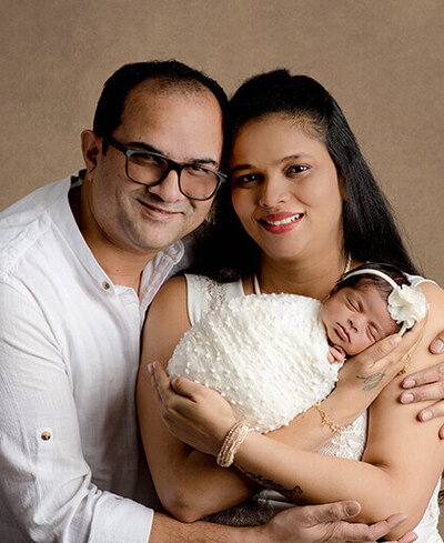 Mom and dad wearing white while holding their new baby who is swaddled. 