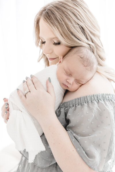 Woman in teal dress holding newborn baby in white wrap on shoulder