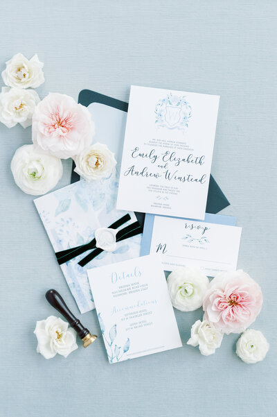 Dusty blue wedding invitation suite on a blue styling mat with flowers.