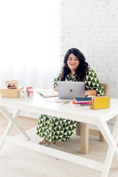 Marissa Martinez in a green and white patterned dress working at a white table with her laptop and Bible