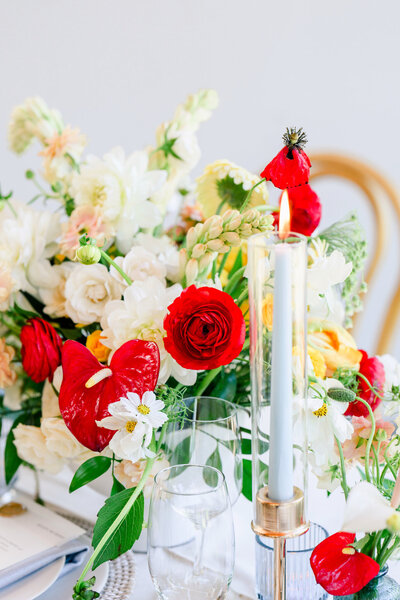 Close-up of a vibrant wedding table centerpiece with red and white florals and a lit candle, styled by a wedding planner in Austin TX.