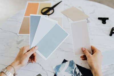Woman holding light blue color swatches next to a beige color swatch.