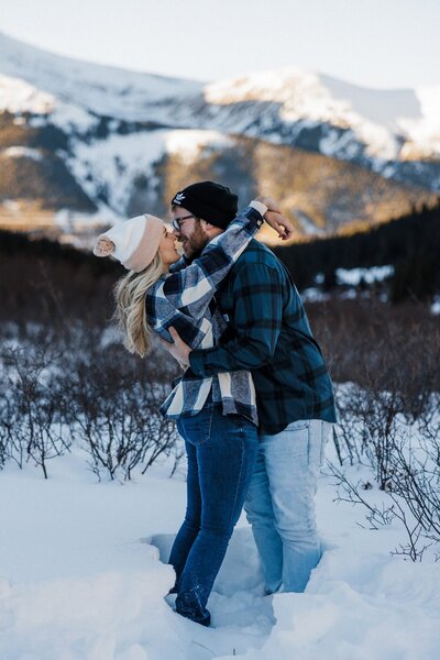 Engaged couple kisses in front of mountain backdrop during Colorado engagement photos.
