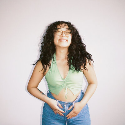 Asian woman smiling with curly hair and light green crop halter top and blue jeans