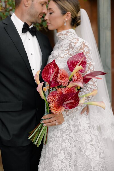 Close-up of bride and groom holding a bold tropical bouquet, foreheads touching