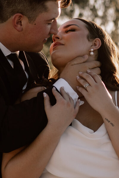 bride and groom hugging while leaning against limo