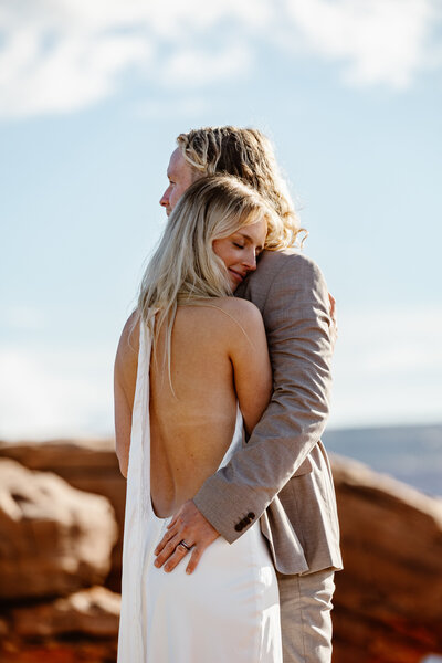 A bride and groom during their elopement in Moab at Dead Horse State Park. The couple is embracing, and the bride has her face resting on the shoulder of the groom. 