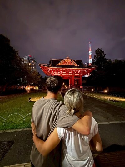 A couple embracing while enjoying a romantic night tour in Tokyo, with Tokyo Tower glowing in the background – experience curated by Tokyo Luxe Drive.