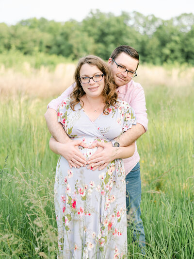Mom in floral dress and dad with arms around Mom in tall grass.