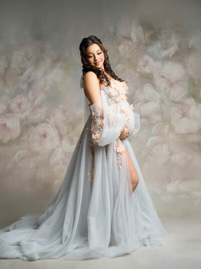 Maternity portrait of petite brunette woman wearing a light blue gown with flowers