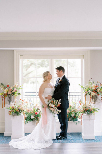 Bride and groom standing at floral altar near bright windows at indoor wedding ceremony in Oakville