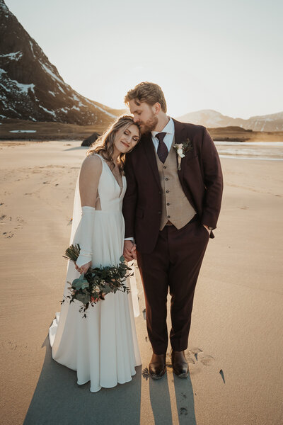 Wedding couple leaning on each other on a beach at sunset in Lofoten