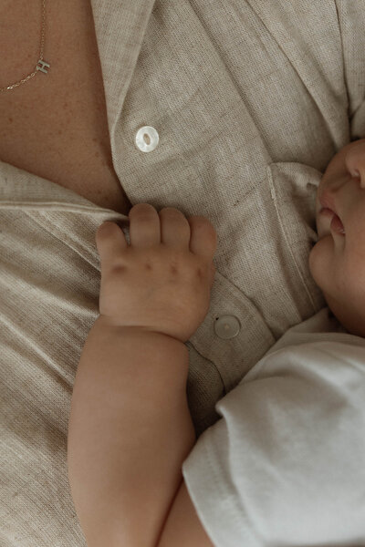 Tender close-up of a baby grasping their parent's shirt, showcasing the deep bond and warmth between mother and child in a natural, heartfelt moment