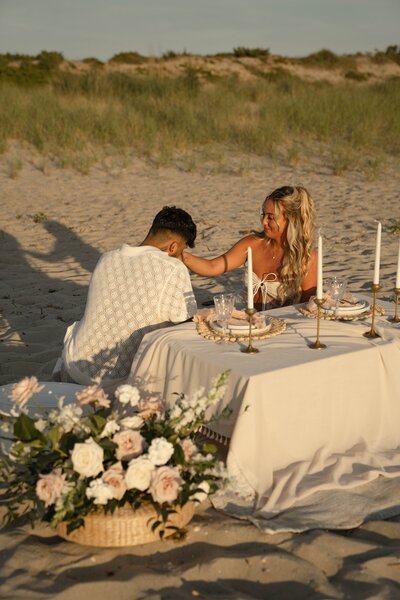 Couple sharing an intimate beachside picnic with candles, elegant table settings, and floral arrangements, styled by Yours Truly, a wedding planner and designer in New Jersey.
