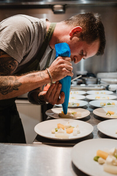 Chef piping a cream component onto multiple vegetable-forward starters at Sael Birmingham restaurant.