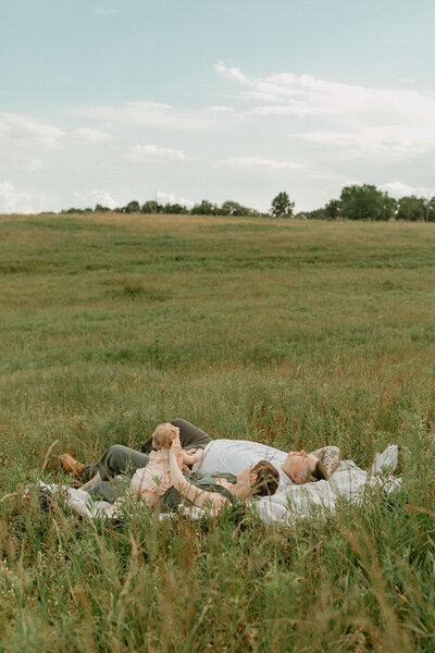 Family of three laying in green field.