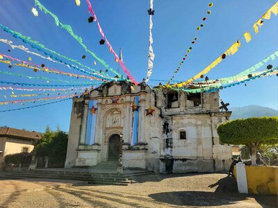 Weathered colonial church adorned with colorful papel picado against a bright blue sky in Chichicastenango, outside Antigua ©Stephanie Dosch | theViatrix Guatemala Private Luxury Travel