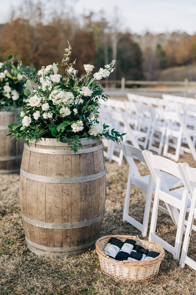 wooden barrel with green and white floral centerpiece on it and white chairs behind it in rows