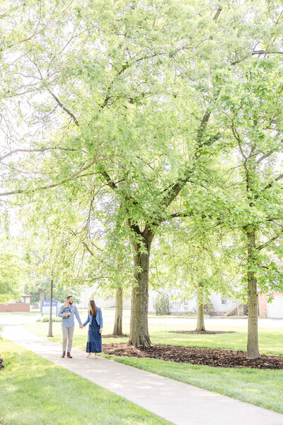 Family walking holding hands on the sidewalk under trees at Cedarville University in Ohio.