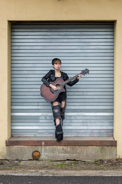 Branding photo of a musician with a guitar in front of steel door